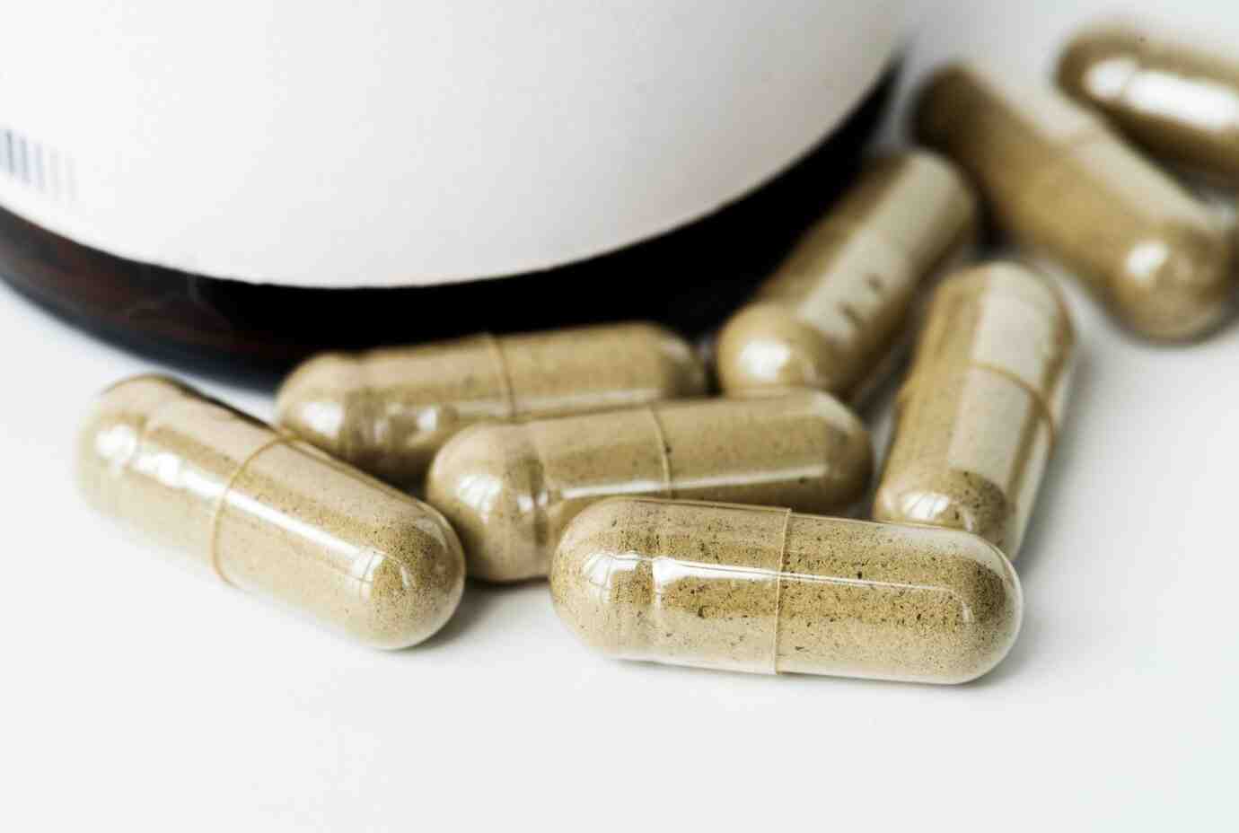 A collection of beige capsules scattered near a dark container, suggesting dietary supplements or herbal products on a white background.