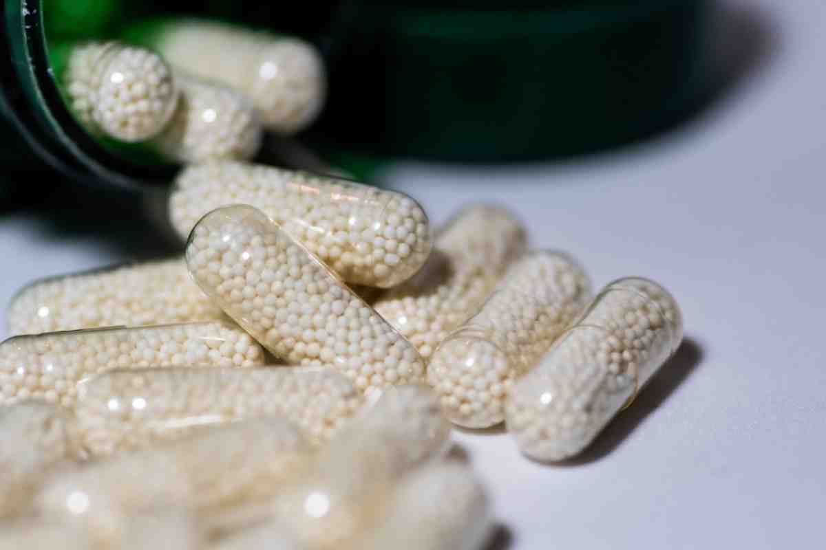 A close-up of translucent capsules filled with small white pellets, spilled from a green bottle on a white surface.