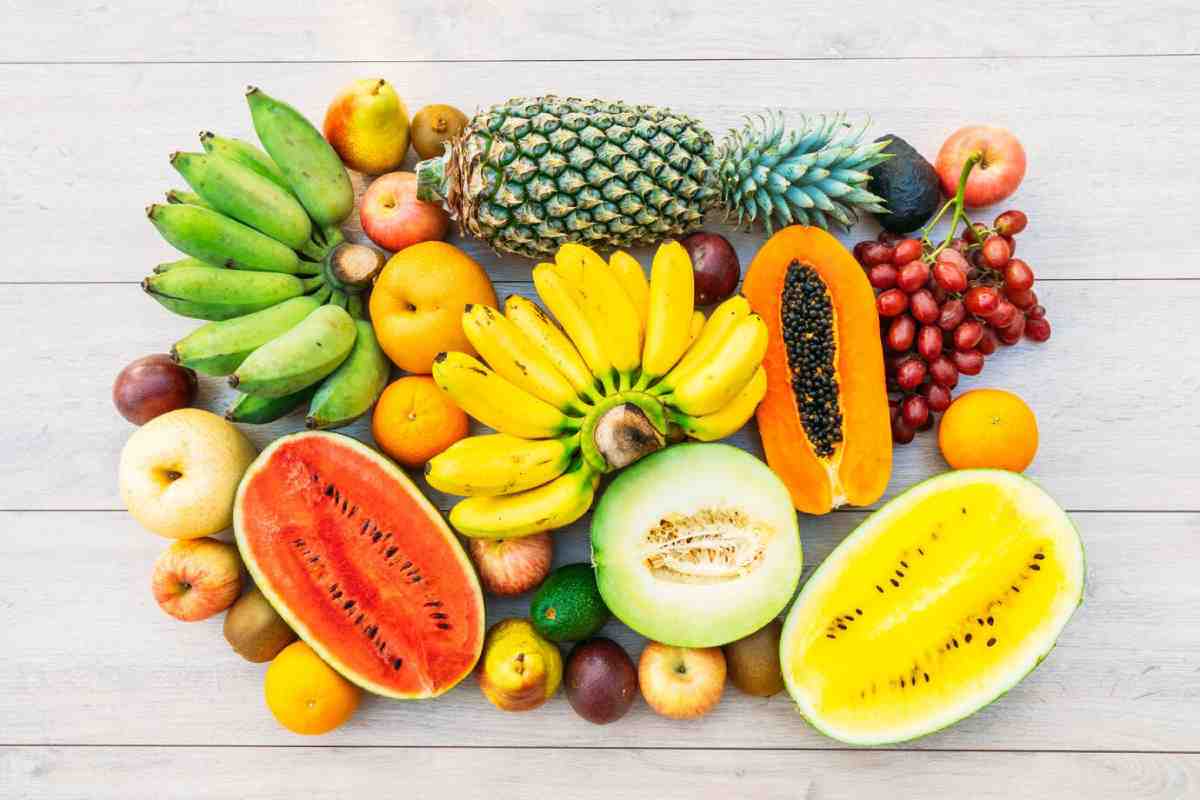 A vibrant assortment of fruits including bananas, watermelon, papaya, grapes, pineapple, and apples arranged on a light wooden surface.